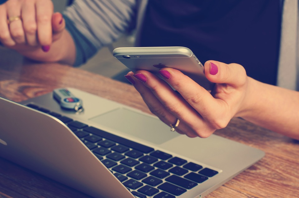 Woman on cell phone in front of laptop.