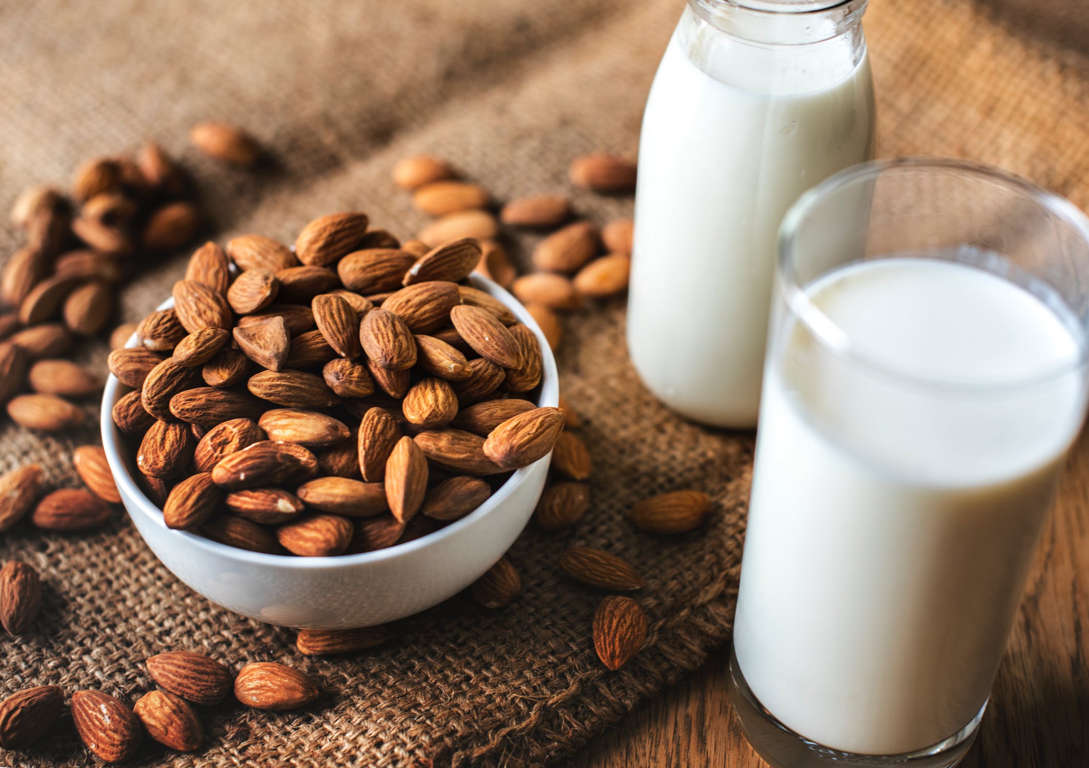Bowl of almonds next to two glasses of almond milk.