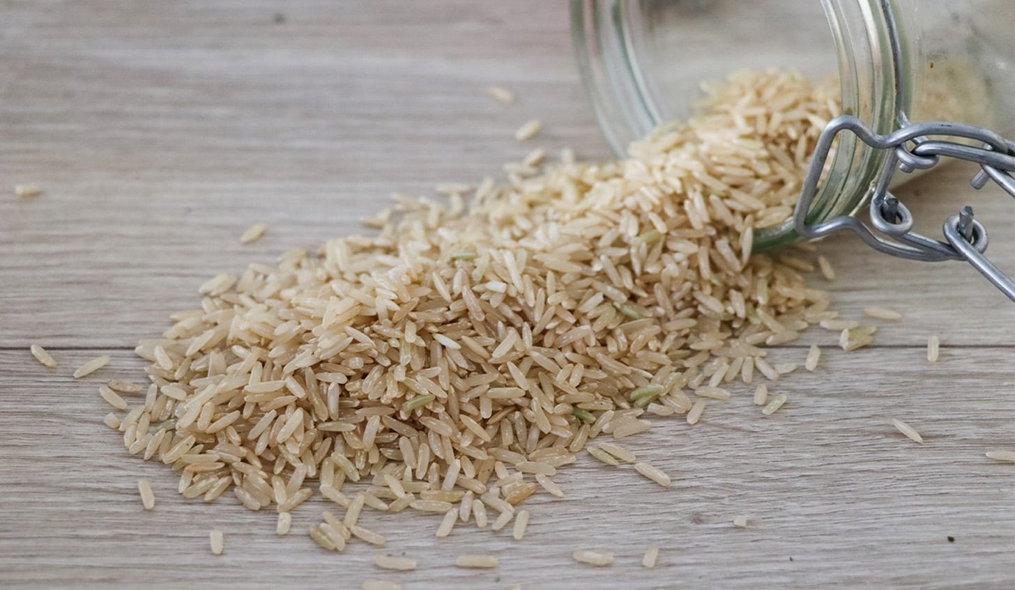 Brown rice grains spilled out of mason jar on counter.