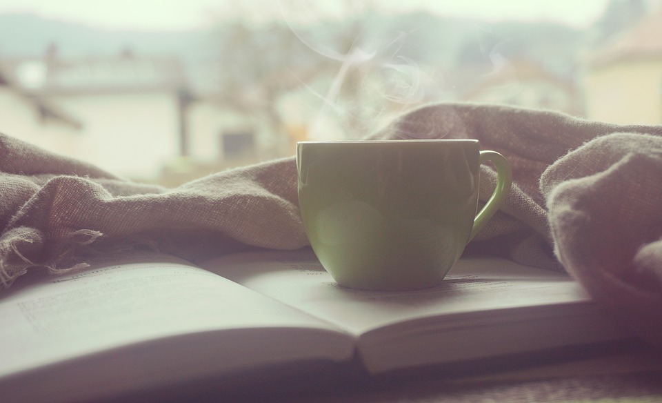 Steaming cup of coffee on top of an open book.