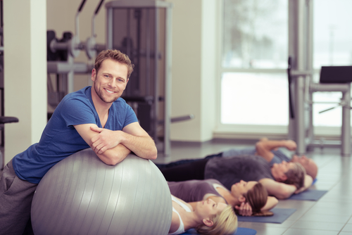 Personal trainer on exercise ball next to yoga class participants.