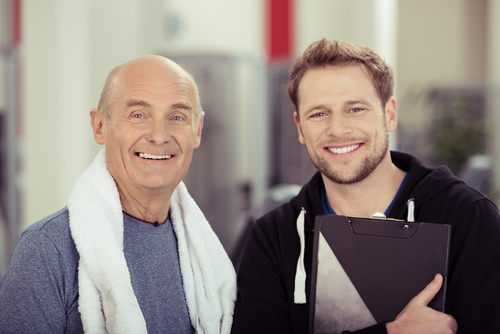 Older man and personal trainer with gym towels around their necks.