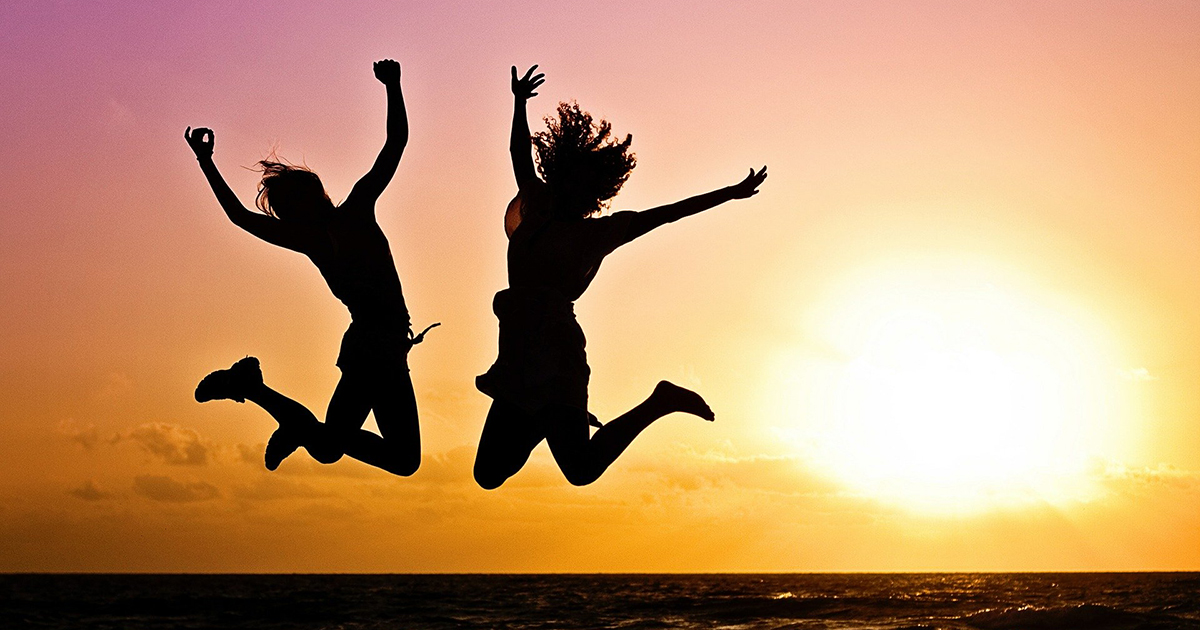 Two people jumping in the air at sunset on a beach.