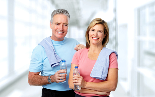 Older couple smiling with gym towels and water bottles.