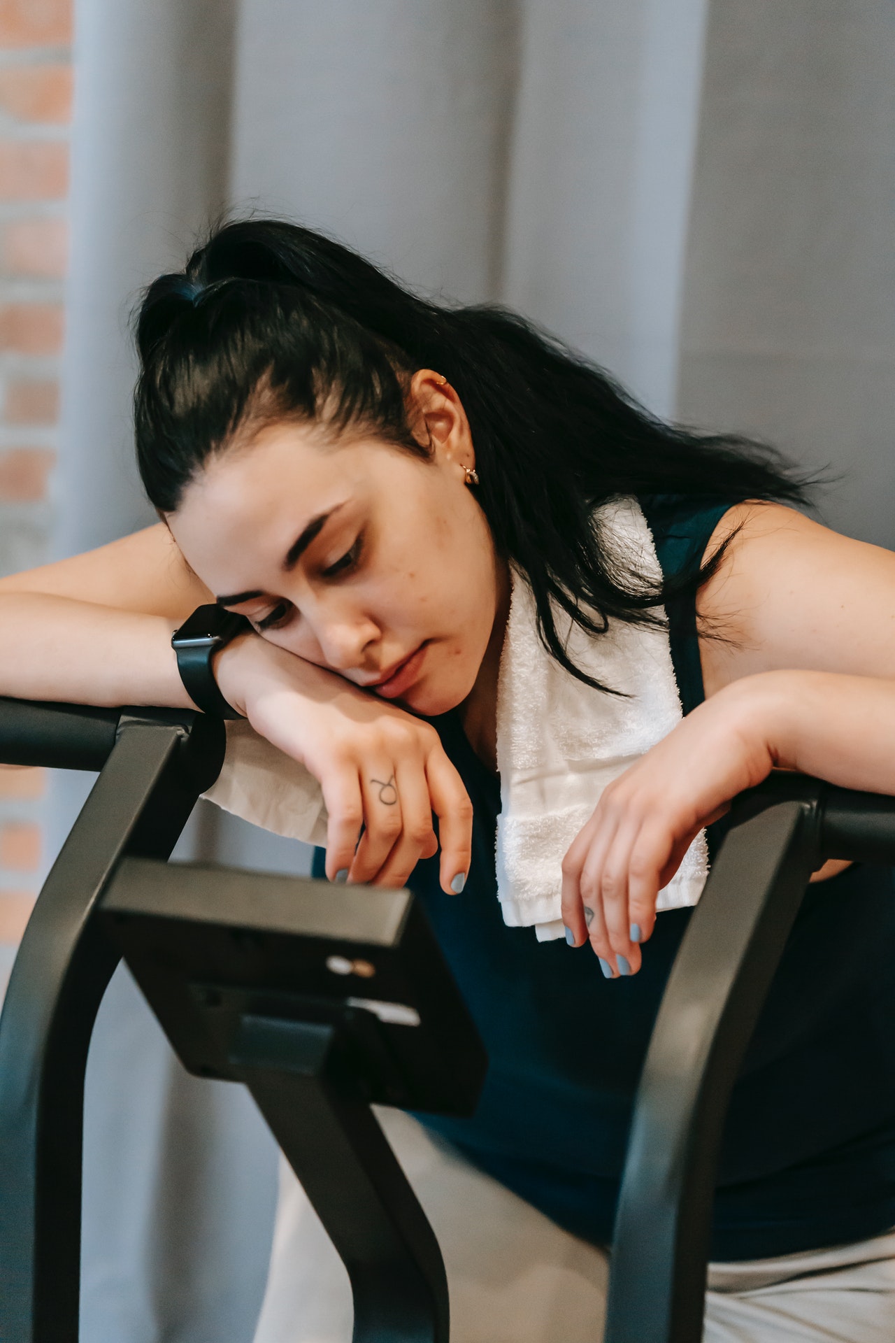 Woman resting arms and head on treadmill with towel around neck.