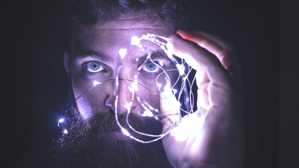 Man holding ball of string lights in front of his face.