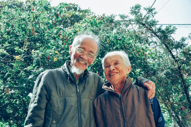 Older couple embracing in garden scenery.