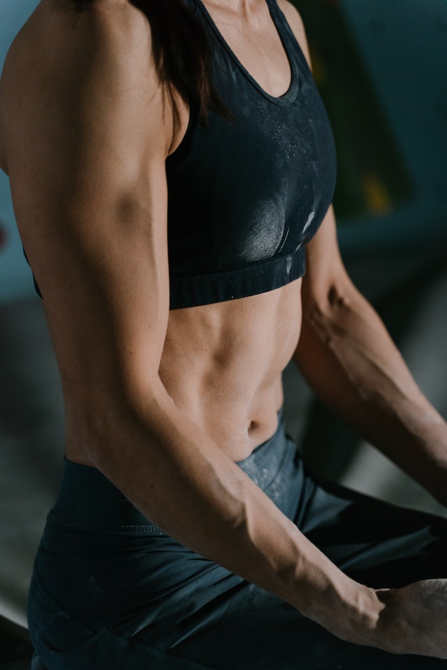 Woman in workout attire flexing arms and abs.