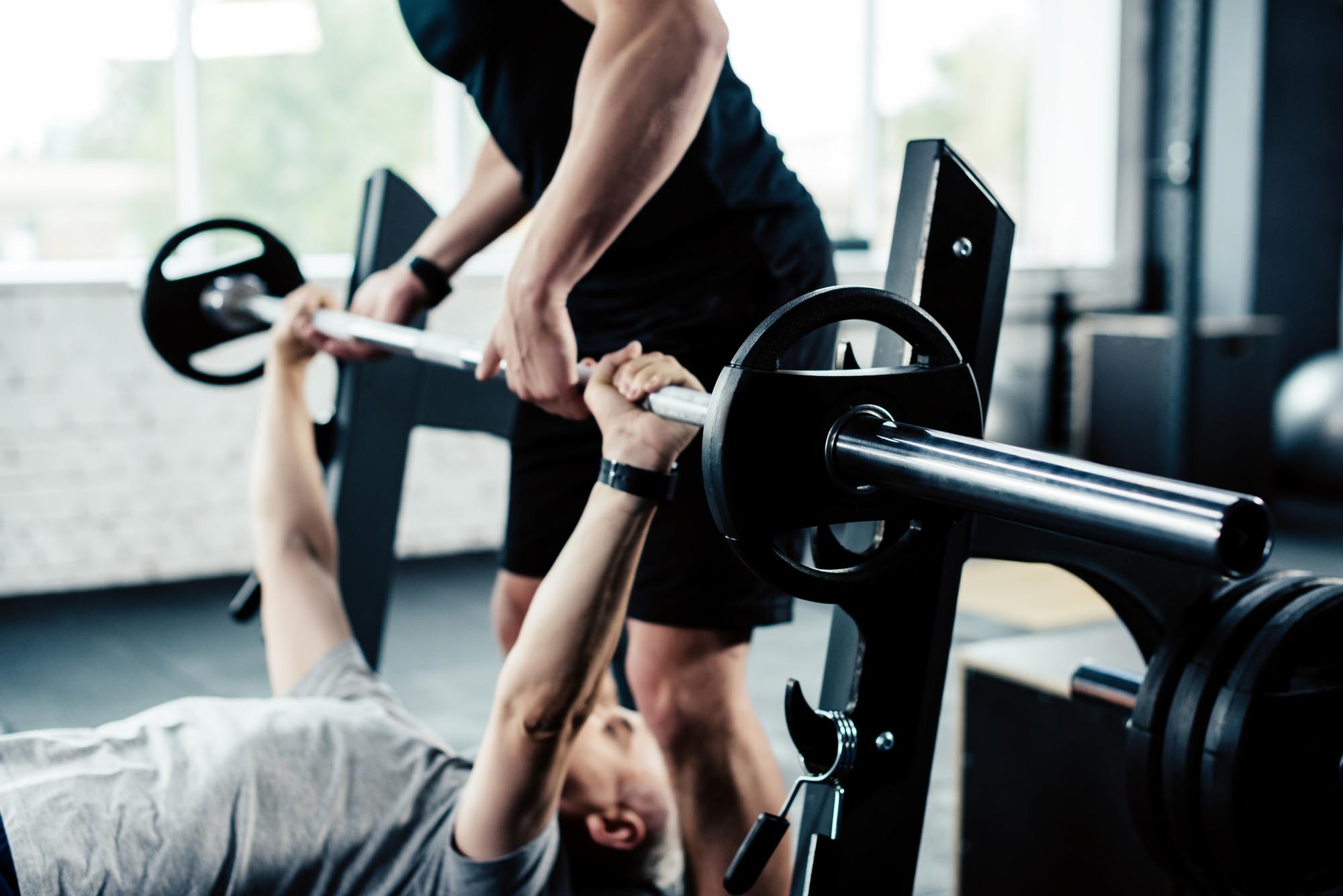 Older man deadlifting with personal trainer spotting.