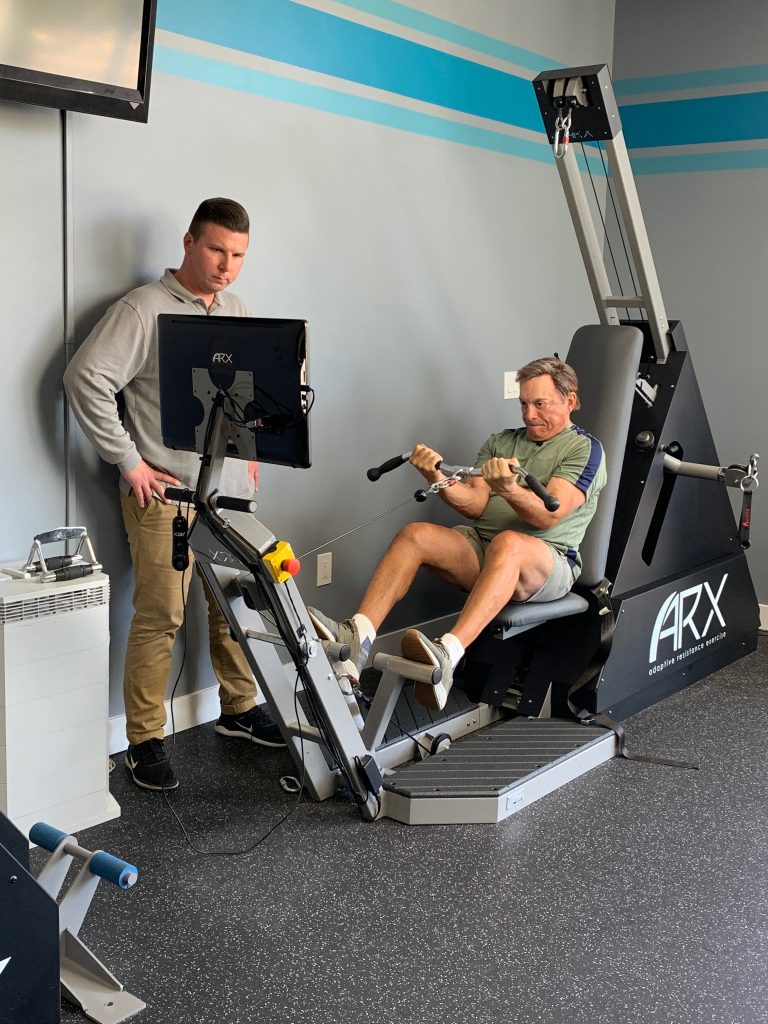 Man working out on ARX machine at Leo's Fitness Lab with personal trainer.
