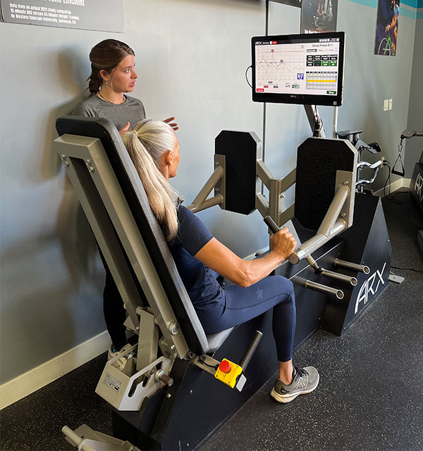 an image of a woman using an ARX exercise equipment machine being instructed by a personal trainer