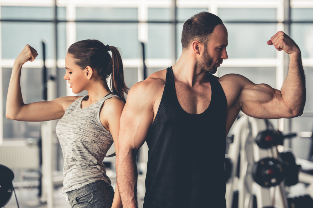 Woman and man flexing biceps back-to-back in a gym