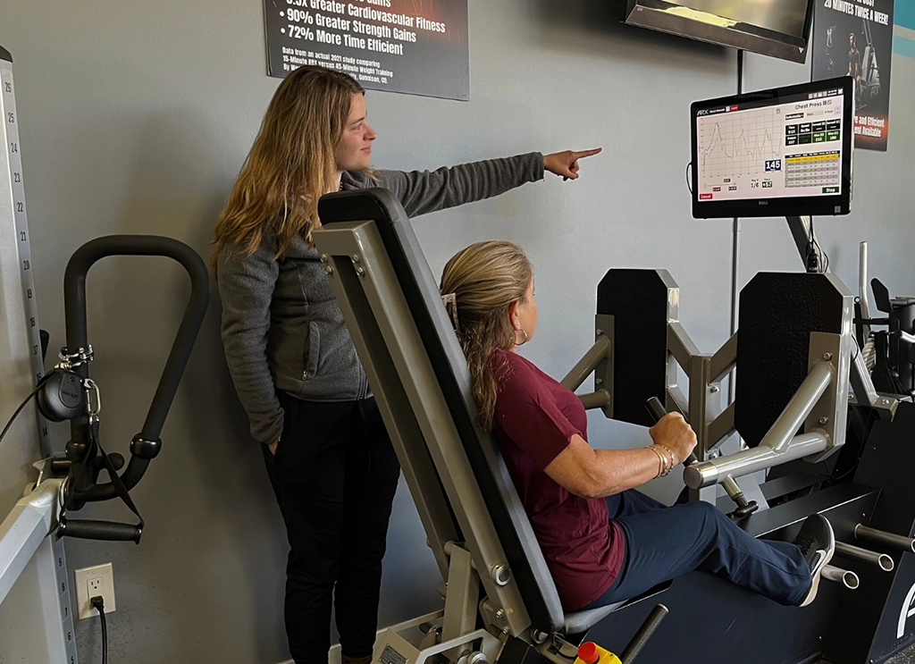 Fitness trainer instructing client on proper form while using chest press machine in gym