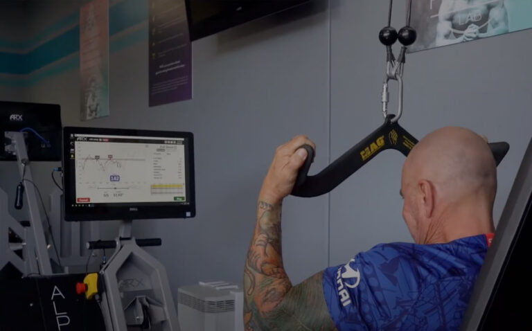 Person with tattoos performing resistance training exercise using suspension straps while monitoring workout data on screen