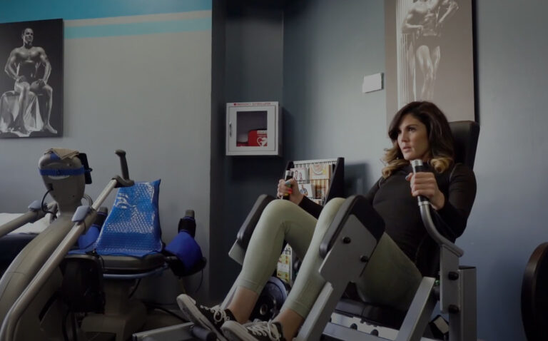 Woman using leg press machine in home gym with blue and gray decor and fitness posters on walls