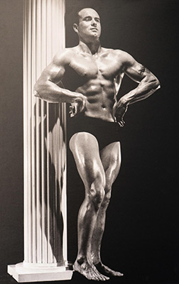 Muscular bodybuilder posing beside classical column in vintage black and white photograph