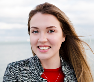 a headshot of a woman with brown hair that is blowing in the wind to the right, she is smiling at the camera