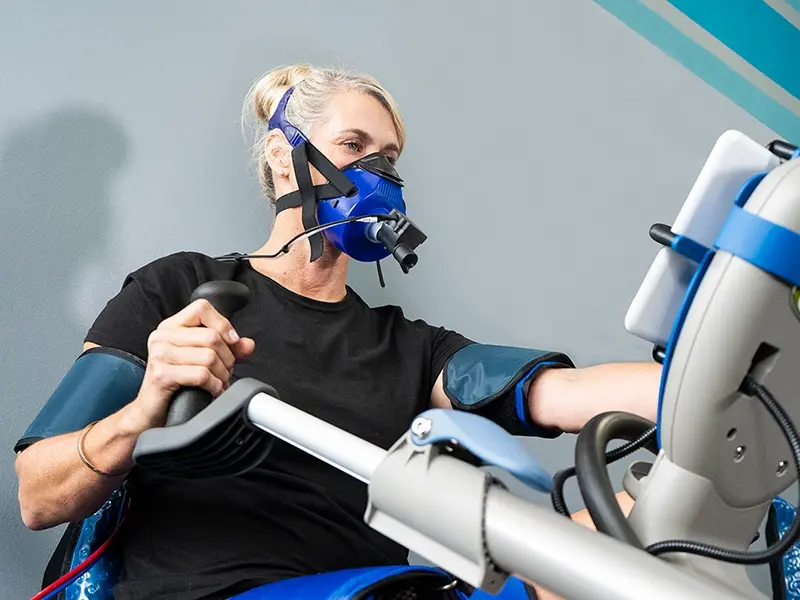 A woman exercises on a Vasper Machine while wearing an oxygen therapy mask designed to alternate between oxygen-rich and oxygen-poor air.